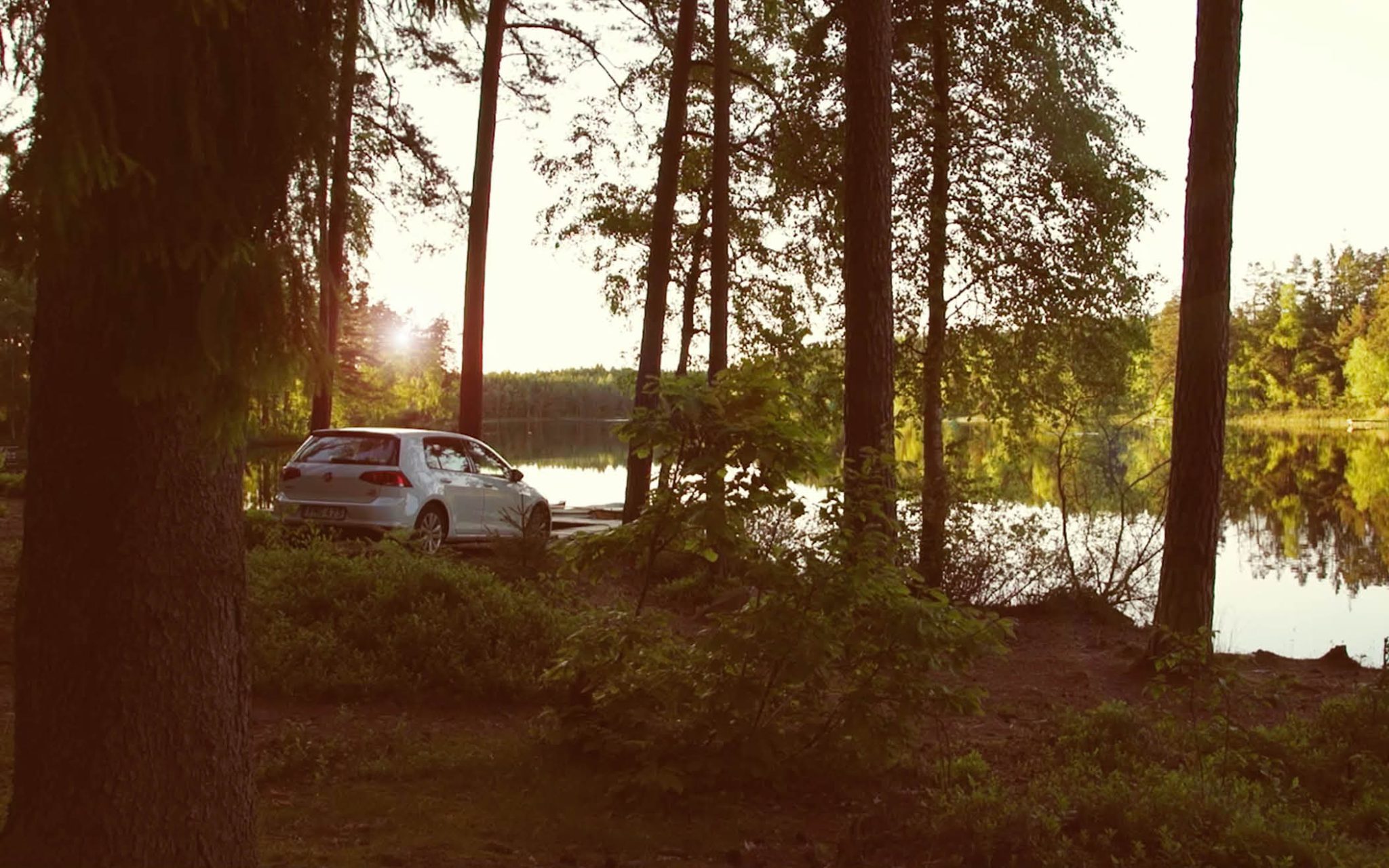 Vit bil parkerad i skogen vid sjökanten vid solnedgången
