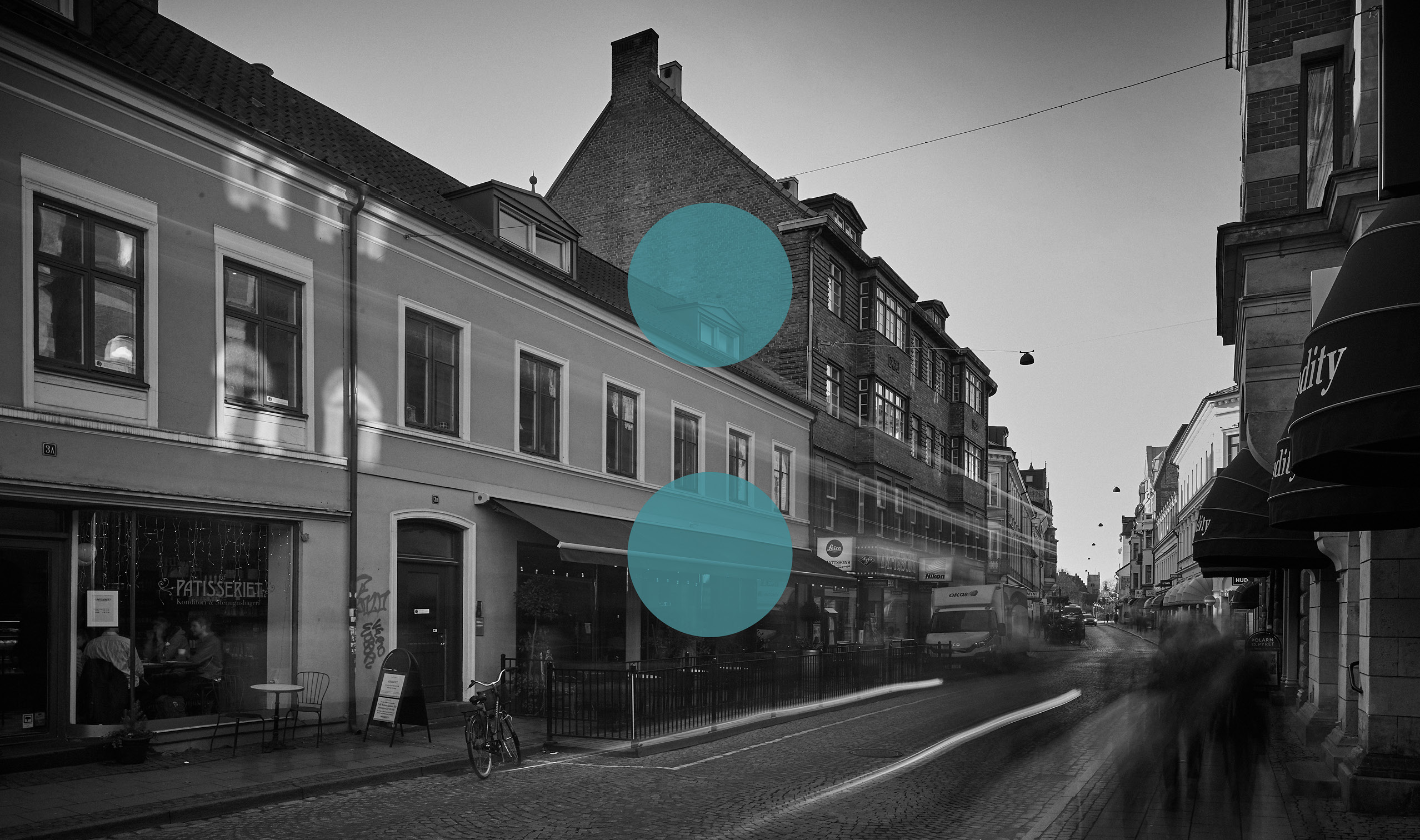 Svartvit bild med två blå prickar för vici advokatbyrå på en gata med rörelse